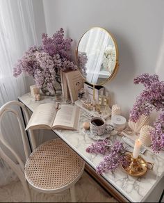 a vanity with flowers and candles on it next to a mirror, candle holder and book