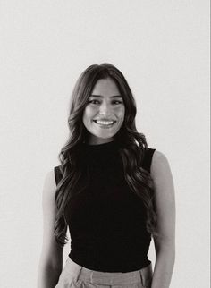 a black and white photo of a woman smiling for the camera with her hands in her pockets