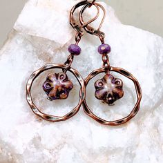 Purple glass flowers floating inside twisted copper rings make these Boho dangle earrings extra special. Copper rings frame the flower beads that have shades of purple, lavender and a Picasso finish.  Lightweight and versatile, these cute earrings will add a pop of color and sophistication to your look.  Custom ear wire style choice at checkout. Hypoallergenic ear wires (nickel and lead free).  Free gift packaging included. Earrings are carded and in an organza bag. Artisan glass beads produced Bronze Czech Glass Dangle Jewelry, Hypoallergenic Flower-shaped Metal Jewelry, Adjustable Copper Flower Earrings, Copper Jewelry With Matching Round Bead Earrings, Artsy Copper Drop Earrings, Adjustable Circular Copper Jewelry, Artsy Nickel-free Copper Earrings, Unique Metal Flower Jewelry, Unique Flower Shaped Metal Jewelry