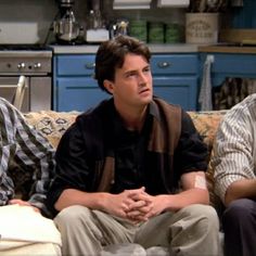 three men sitting on a couch in a kitchen