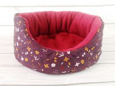 a purple dog bed sitting on top of a white wooden floor next to a red pillow