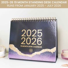 a desk calendar sitting on top of a table next to a cup and candle holder