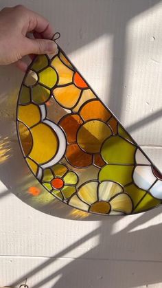 a hand is holding a stained glass hanging light fixture in the shape of a tear