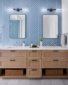 a bathroom with two sinks and mirrors on the wall next to each other in front of blue herringbone tiles