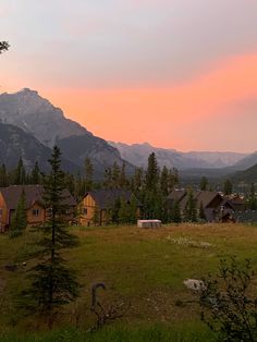 the sun is setting over mountains and houses in the foreground with trees on either side