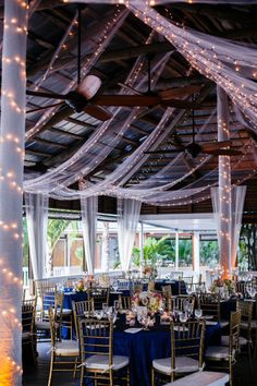 an indoor wedding venue with blue linens and white draping on the ceiling