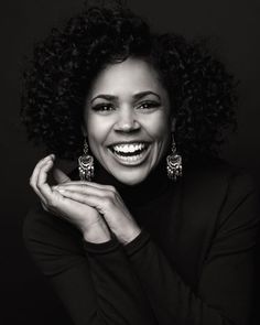 a woman smiling with her hands on her chest and wearing earrings in front of her face