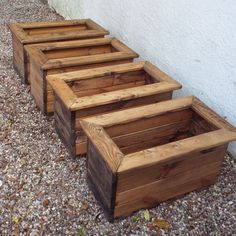 four wooden planters lined up against a wall on the side of a building with gravel