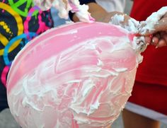 a person holding a cake with white frosting on it and pink icing on the top