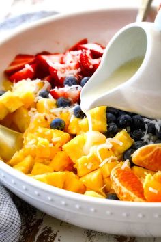 a bowl filled with fruit and milk being poured into it's side, on top of a table