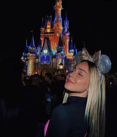 a woman standing in front of a castle at night with her eyes closed and the lights on