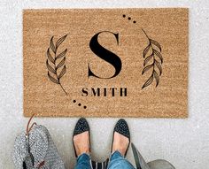 a person standing in front of a door mat with the letter s and leaves on it