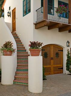 a house with stairs and potted plants on the front steps, along with two large planters filled with flowers