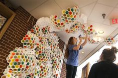 two women are decorating a wall with plastic cups and paper tubes in the shape of flowers