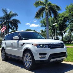 the white range rover is parked in front of some palm trees and an american flag