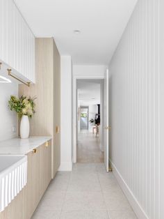 a long hallway leading to a kitchen with white walls and floor tiles on both sides