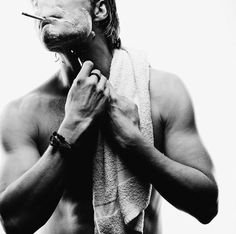 a shirtless man is holding a towel over his face and brushing his teeth with an electric toothbrush