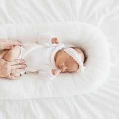 a woman holding a baby in her arms on top of a white bed with pillows