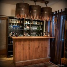 a bar with several bottles and glasses on it in a room that has curtains hanging from the ceiling