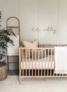 a baby crib with a blanket and pillows on it next to a potted plant