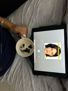 a person sitting on a bed with a cup of coffee and an ipad next to them