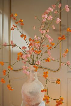 a vase filled with pink and orange flowers on top of a white cloth covered table