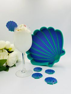 there is a drink in a glass next to some blue fan shaped plates and flowers