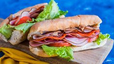 two sub sandwiches sitting on top of a wooden cutting board