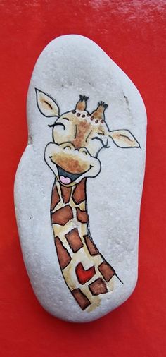 a painted rock with a giraffe's face on it, sitting on a red surface