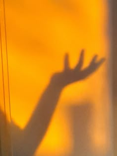 the shadow of a person's hand on a window sill in front of a yellow wall