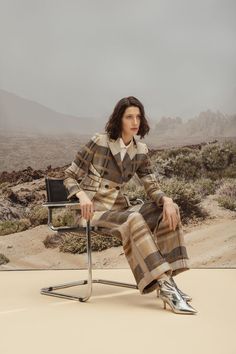 a woman sitting on a chair in front of a desert landscape with mountains behind her