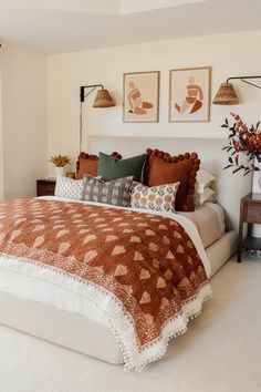 a bed with pillows and blankets in a bedroom next to two pictures on the wall