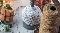 two balls of twine sitting next to each other on a white wooden surface with christmas lights in the background