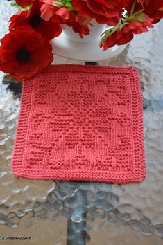 red flowers are in a white vase with a pink knitted placemat on a table