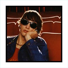 a man wearing sunglasses sitting in front of an empty theater seat with his hand on his chin