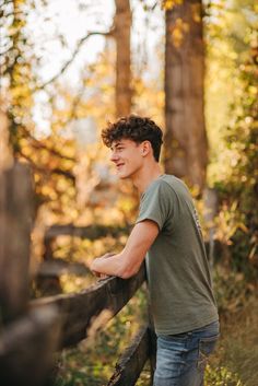 a young man leaning on a fence in the woods