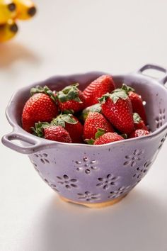 a purple colander filled with strawberries on top of a white table next to bananas