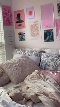 an unmade bed with pink and white sheets, pillows and pictures on the wall