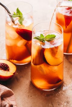 two glasses filled with iced tea and peaches next to sliced peaches on a white table