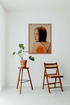 two wooden chairs in front of a white wall with a painting hanging on the wall