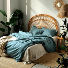 a bed with blue sheets and pillows in a room next to potted plants on the floor