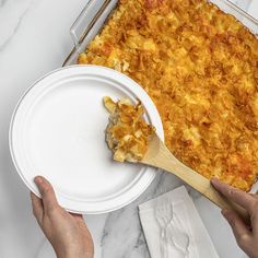 a person holding a plate with a casserole on it and a wooden spatula