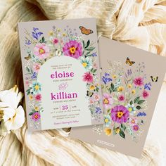 two wedding cards with flowers and butterflies on them, sitting next to a flower bouquet