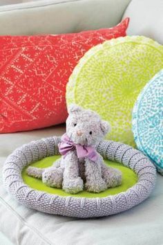 a teddy bear sitting in a pet bed on a couch next to pillows and cushions