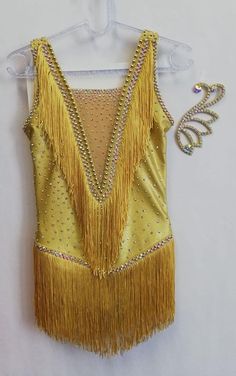 a yellow top with fringes and sequins hanging on a hanger next to a pair of scissors