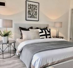 a bedroom with white walls and grey bedding, two lamps on either side of the bed