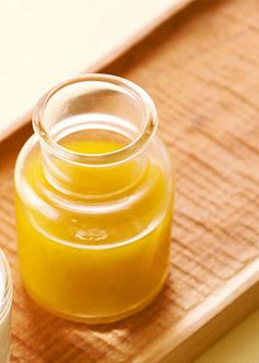 two jars of yellow liquid sitting on top of a wooden cutting board next to an empty container