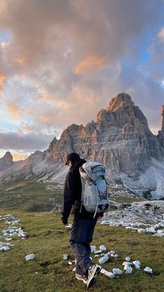 a man with a backpack is walking on the grass in front of some mountain peaks