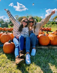 two women sitting on the ground in front of pumpkins with their arms spread out