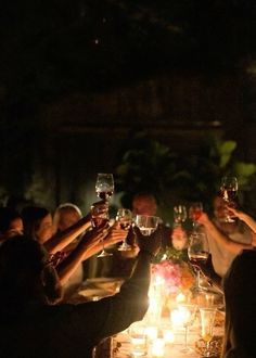 a group of people toasting wine glasses at a dinner table with candles in front of them